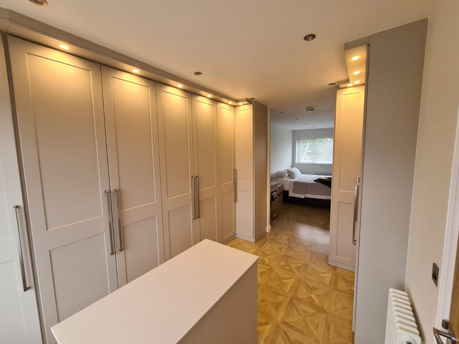 Custom, fitted wardrobes built in to a section of a bedroom to create a new dressing room /walk-in wardrobe area. Integrated lighting, shaker style doors with silver long handles and off-white finish to the panels. 